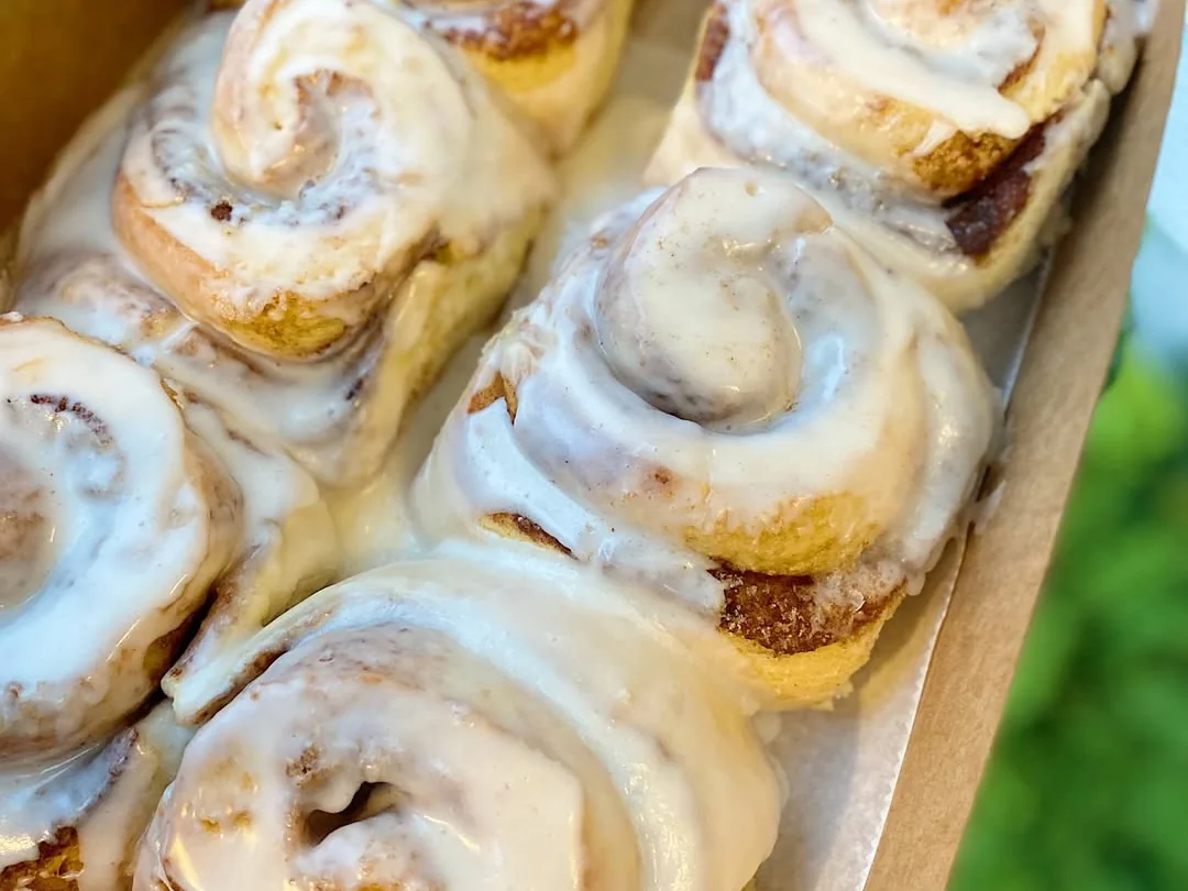 Box of large cinnamon rolls covered with white icing.