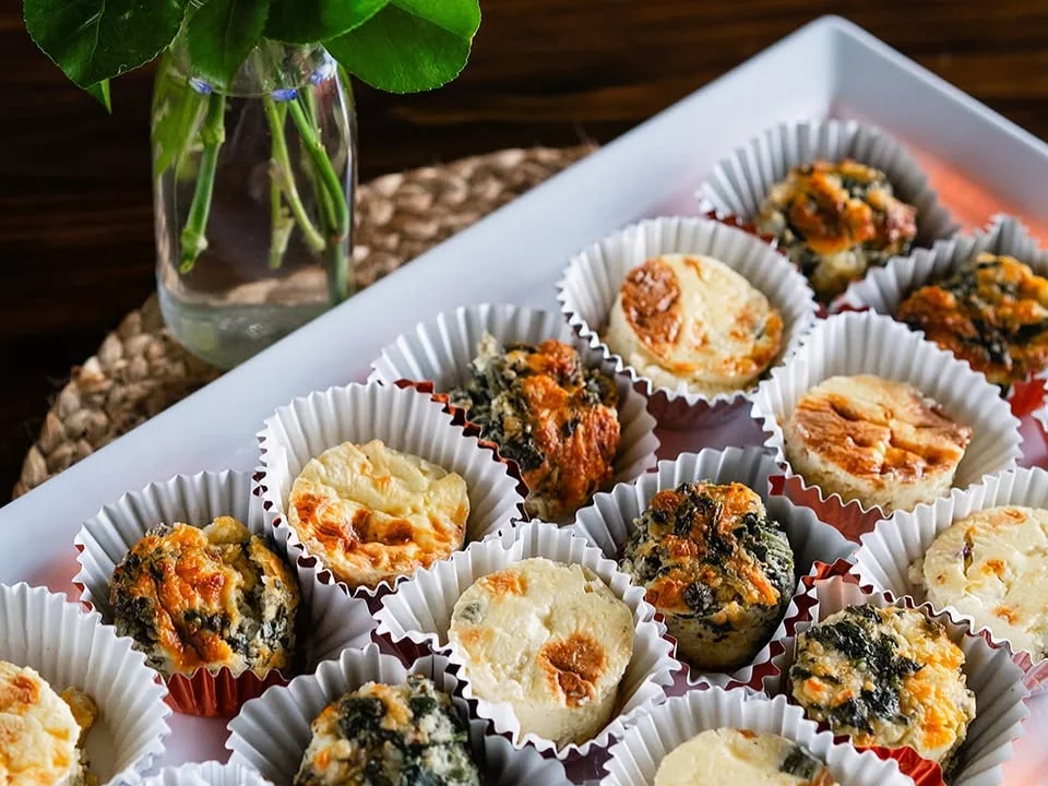 Assorted bite-size desserts arranged in paper cups on a white tray.