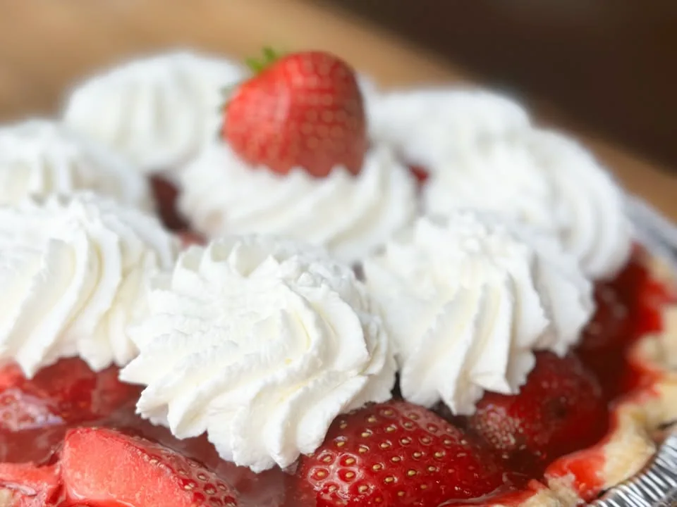 Pie topped with whipped cream and sliced strawberries.