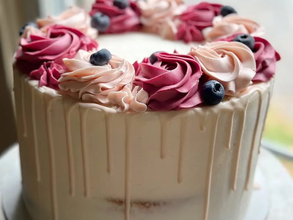 Close view of a white cake with pink icing swirls and berry decorations.